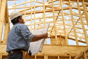 Builder holding a blueprint looking up at the framing of a house